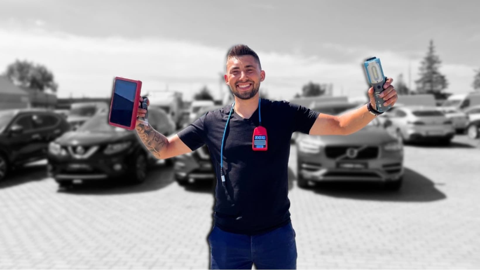 Dawid Uszaruk z testerem diagnostycznym i lampą warsztatową, w tle samochody na parkingu
